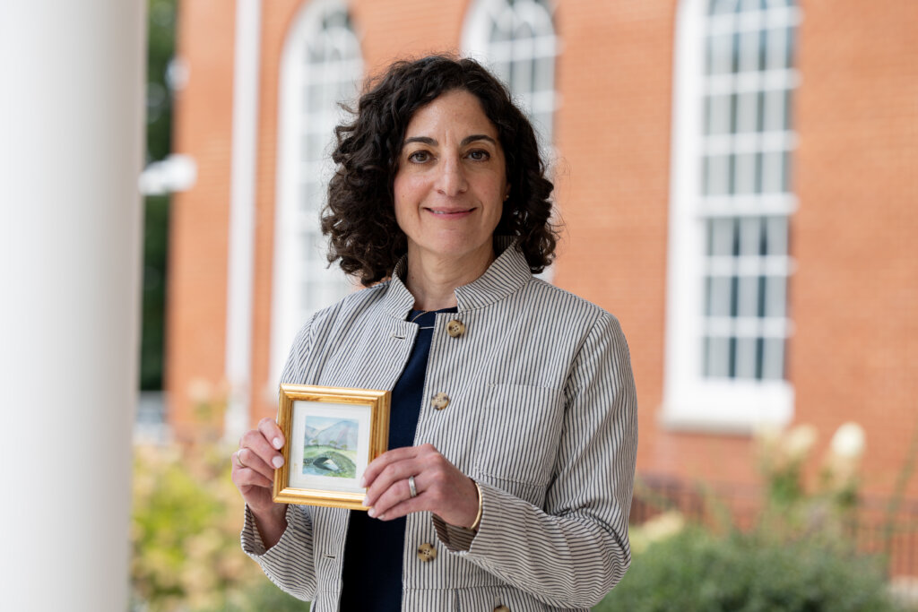 Inaugural Dean, Dr. Melissa Napolitano, holds a watercolor painting of a bridge in front of Seacobeck Hall.